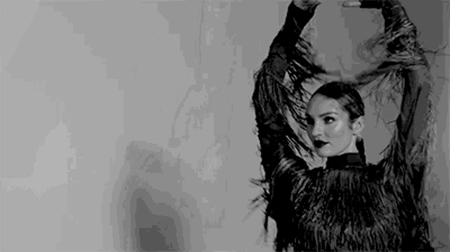 a black and white photo of a woman in a fringed top dancing with her arms in the air .