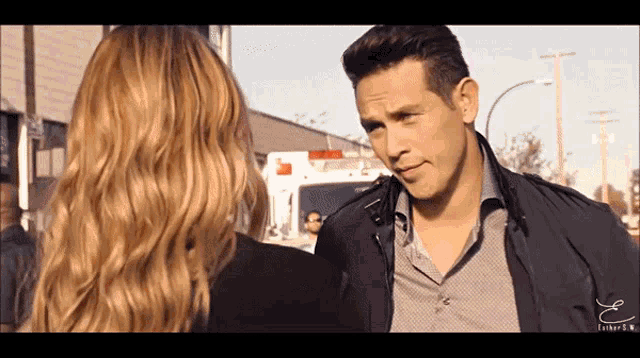 a man and a woman are talking in front of an ambulance with the letter e on the bottom