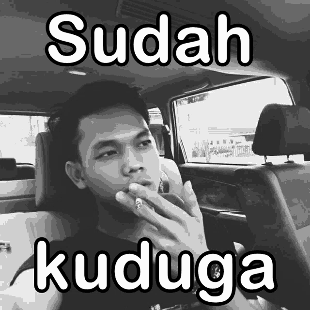 a man is smoking a cigarette in a car with the words sudah kuduga above him