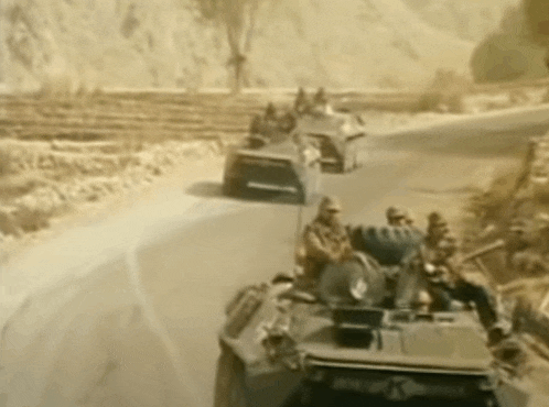 a group of soldiers are driving down a road in a military vehicle .