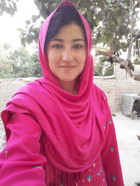 a woman wearing a pink scarf and a pink shirt smiles for the camera