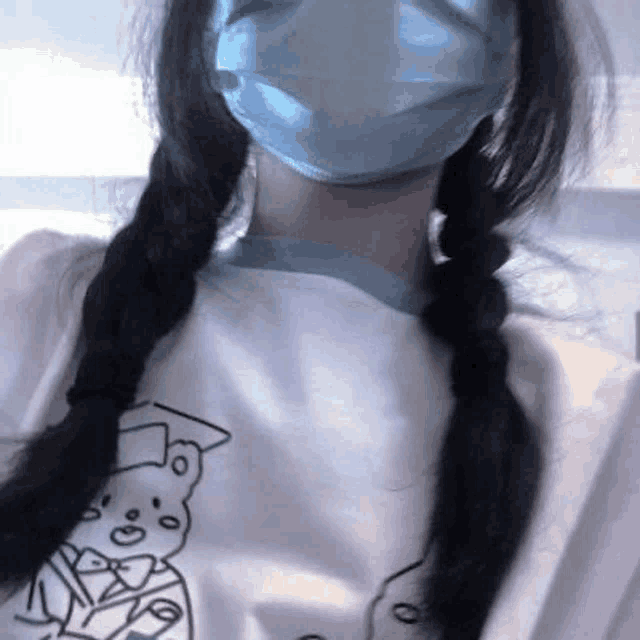 a woman wearing a mask and braids is wearing a white t-shirt .