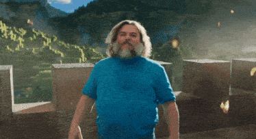 a man with a beard wearing a blue shirt is standing in front of a mountain