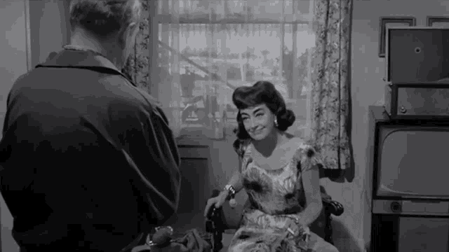 a black and white photo of a woman sitting in front of a television