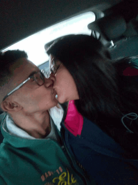 a man and a woman kissing in a car the man is wearing a green jacket that says ' base ' on it