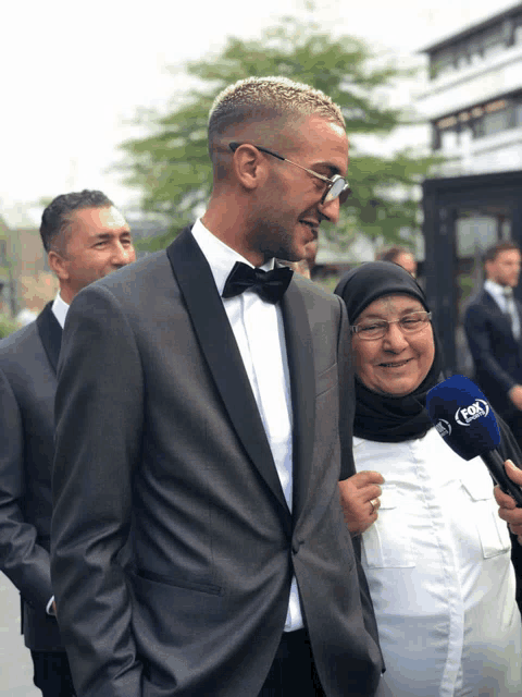 a man in a tuxedo is standing next to a woman with a fox microphone