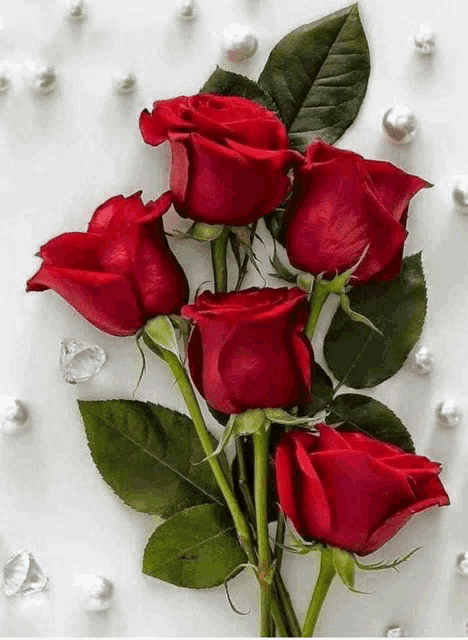 a bouquet of red roses surrounded by pearls and diamonds on a white surface .