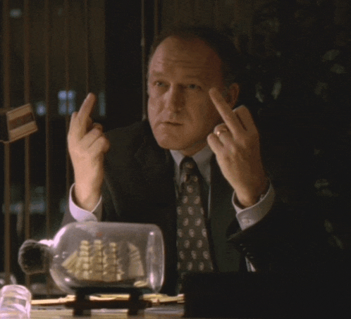 a man in a suit and tie is sitting at a desk giving the middle finger