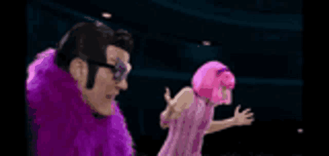 a man in a purple fur coat and a woman in a pink dress are standing next to each other in a dark room .