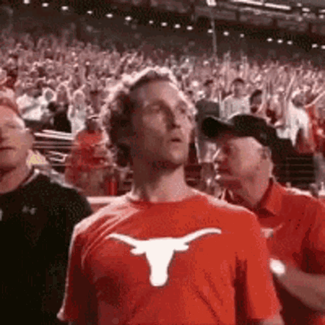 a man wearing a red shirt with a longhorn on it is standing in front of a crowd of people .