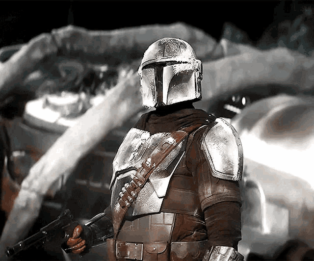 a man in armor is holding a gun and wearing a helmet with a t on it