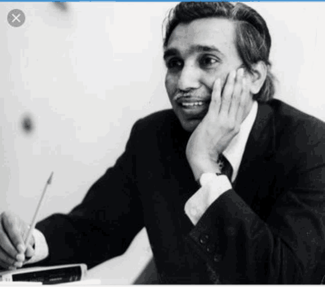 a man in a suit and tie is sitting at a desk with his hand on his face .