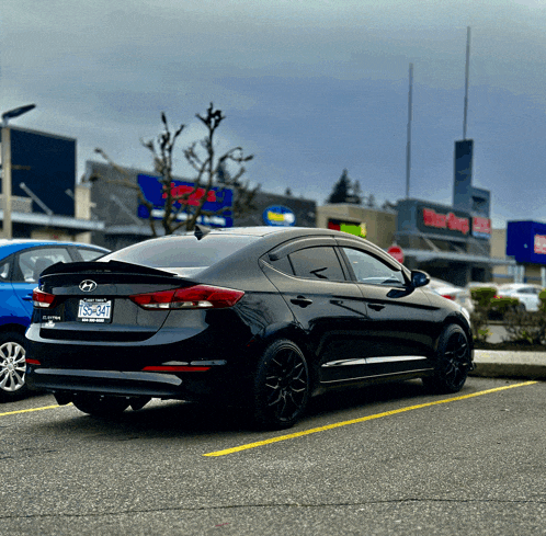 a black hyundai car is parked in a parking lot in front of a store