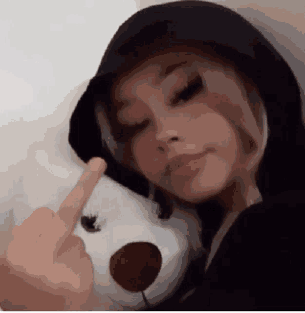 a woman is holding a teddy bear and giving the middle finger .