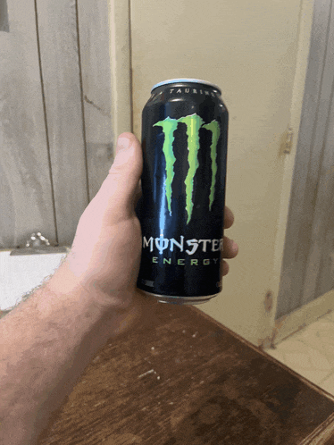 a person is holding a can of monster energy