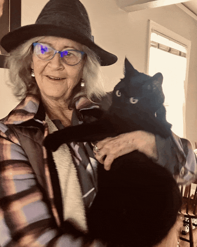 a woman wearing glasses holds a black cat