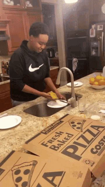 a man in a black nike sweatshirt is washing plates in the kitchen