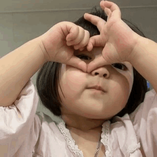 a little girl is making a heart shape with her hands over her face .