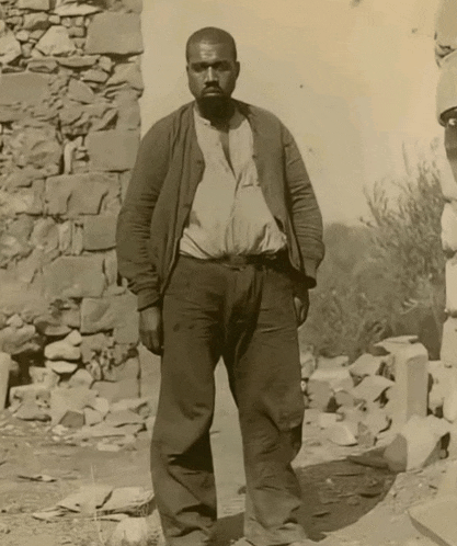 a man standing in front of a stone wall wearing a brown jacket