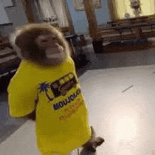 a monkey wearing a yellow t-shirt is standing on a white floor in a room .