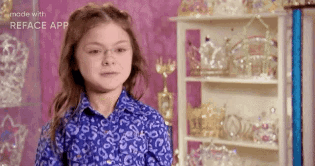 a young girl wearing glasses and a blue shirt is standing in front of a shelf filled with trophies .