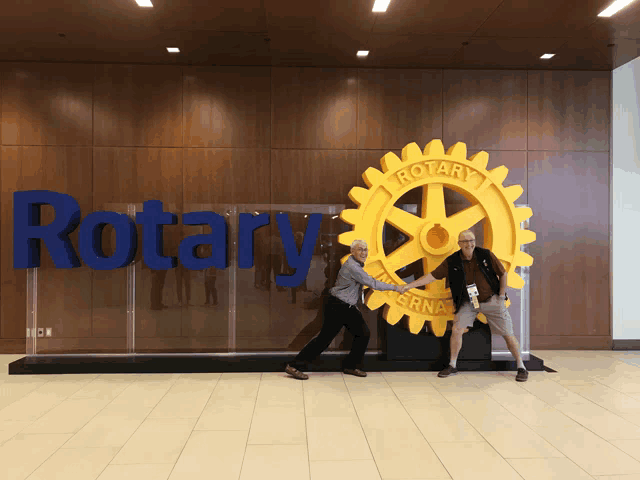 two people standing in front of a large rotary logo