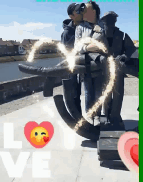 a couple kissing in front of a statue with the word love in the corner