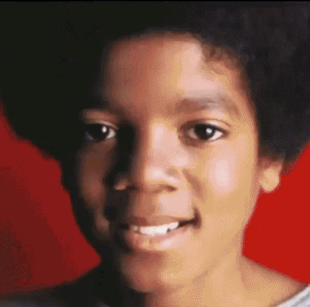 a close up of a young boy 's face with a red background and a smile .