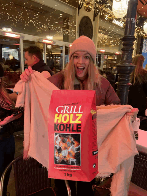 a woman is holding a blanket and a bag that says grill holz kohle