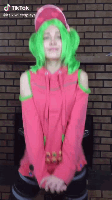 a woman in a pink and green costume is standing in front of a brick wall .