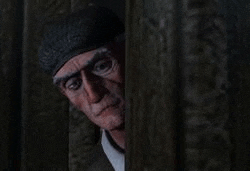 a man is peeking out from behind a wooden fence in a dark room .