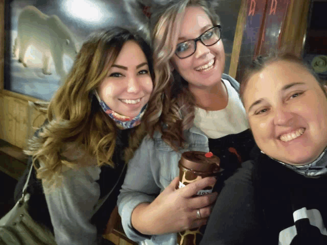three women are posing for a picture and one of them is holding a coffee cup that says ' tiger ' on it
