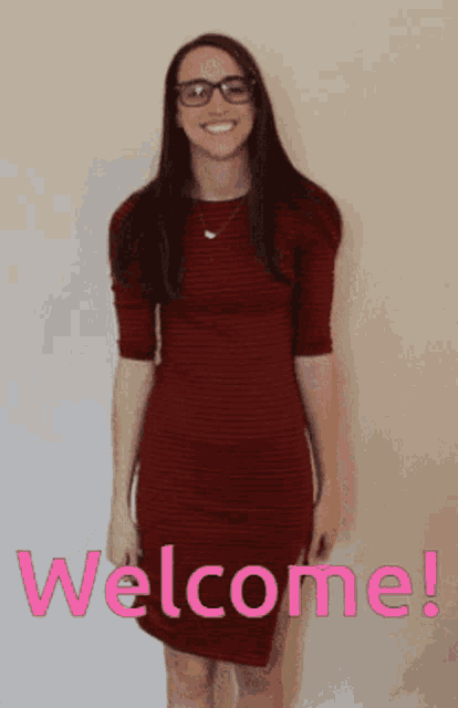 a woman in a red dress is standing in front of a wall with the words welcome written on it