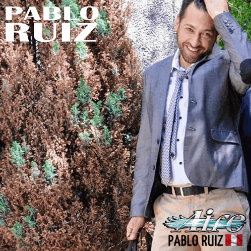 a man in a suit and tie stands in front of a bush with the name pablo ruiz