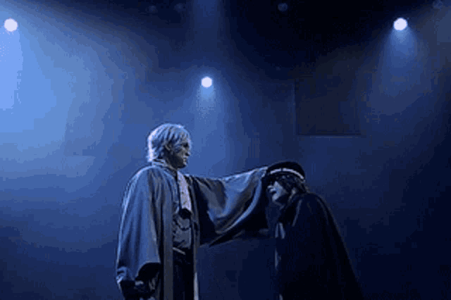 a man in a cape stands next to another man in a black cape