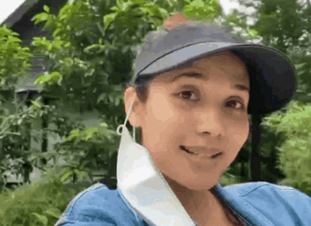 a woman wearing a hat and a mask is smiling and looking at the camera .