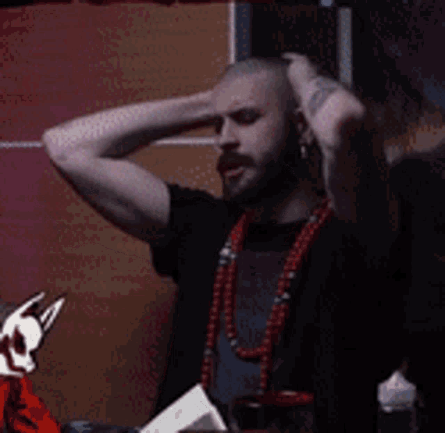 a man wearing a black shirt and a red necklace is holding his head