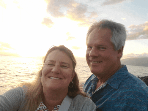 a man and a woman are posing for a picture with the ocean in the background