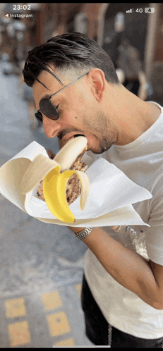 a man is eating a banana wrapped in paper with the time 23:22