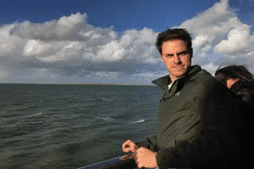 a man in a green jacket stands in front of a large body of water