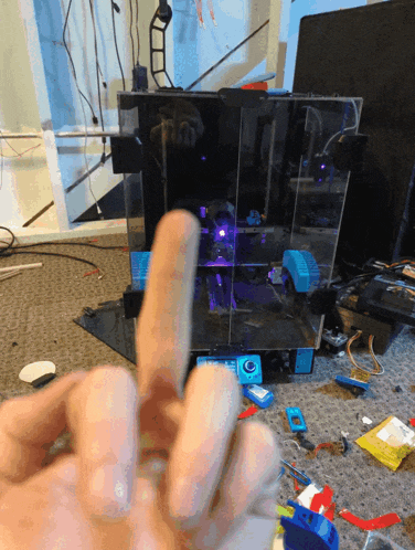 a person giving the middle finger in front of a 3d printer with purple lights