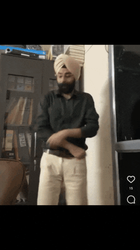 a man wearing a turban and a black shirt is standing in front of a bookcase with binders on it