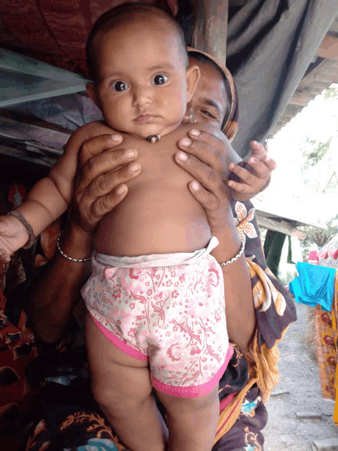 a woman is holding a baby in her arms who is wearing pink shorts