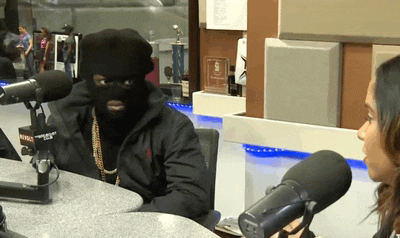 a man wearing a mask is talking to a woman in front of a radio station