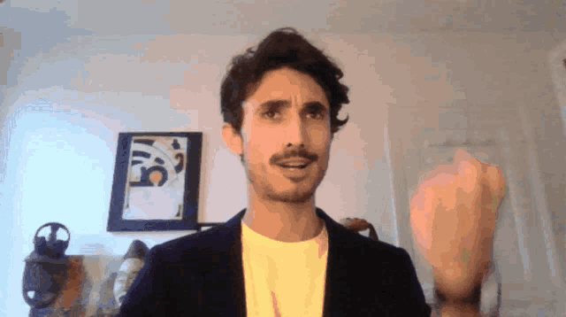 a man with a beard is wearing a black jacket and a yellow t-shirt