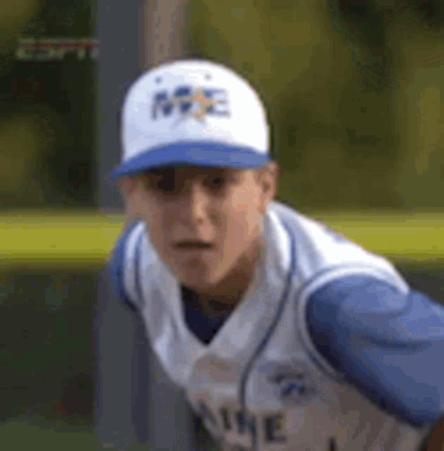 a young man wearing a baseball cap and a blue and white jersey is standing on a baseball field .