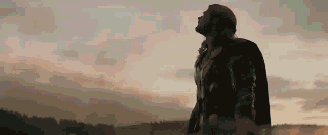 a silhouette of a man in a black coat looking up at the sky