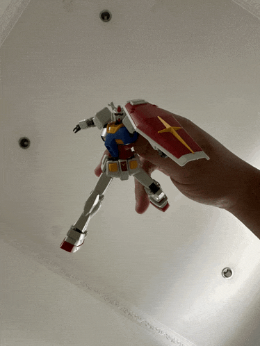 a person is holding a toy robot with a red and yellow cross on its shield