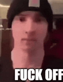 a man wearing a beanie and the words `` fuck off '' is making a funny face .