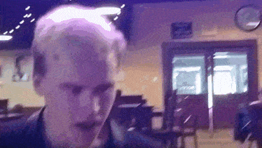 a blurry picture of a man in a room with a clock on the wall behind him